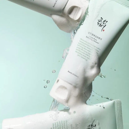 Beauty of Joseon Green Plum Refreshing Cleanser 100ml  - Trois tubes de produits nettoyants Beauty of Joseon disposés de manière dynamique, de l'eau s'écoulant entre eux, créant des éclaboussures et de la mousse, sur un fond vert menthe pâle - Kbeauty Korean skincare Europe fast delivery - Skincare coréenne SKINOREA shop Paris France livraison rapide 